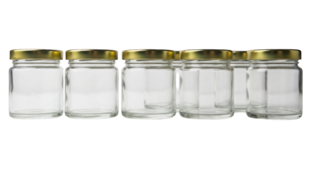 Empty glass jars with golden lids stand lined-up on dark background