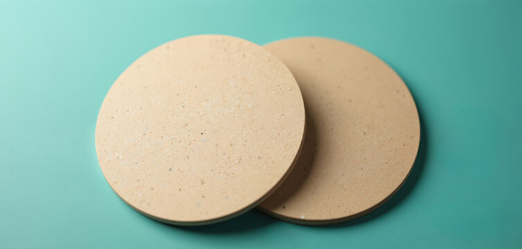 Two round blank coasters lay on bright teal background. Natural beige material shows subtle texture. Simple eco friendly mockup perfect for custom brand design presentations, product marketing