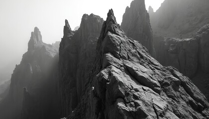 Dramatic black white landscape shows sharp jagged rock peaks. Towering mountain cliffs form rough stone texture. Misty fog atmosphere covers vast rugged nature. Abstract formation creates powerful