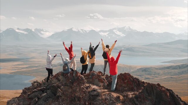 Group of young happy tourists hikers are standing in winner poses with raised open arms at mountain top