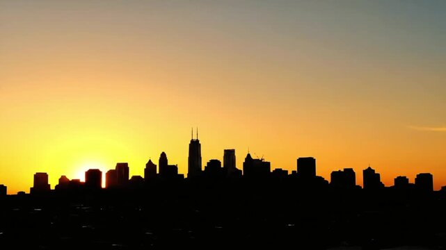 Majestic Chicago city skyline silhouette at golden hour sunset featuring iconic downtown buildings against a vibrant orange and yellow sky perfect for urban est