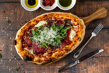 Top view of Neapolitan pizza with bacon, arugula and parmesan on wooden table