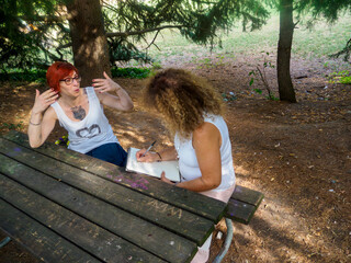 Two women friends enjoying a discussion outdoors at a picnic table in a park on a sunny day
