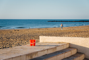 Une personne abandonnant un seau orange sur une plage de sable. Enfance perdue. Solitude à la mer méditerranée. Touriste seul