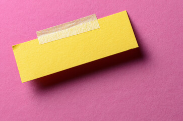 Piece of blank yellow paper note with adhesive sticky tape and shadow on pink background