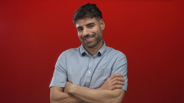 Man with crossed arms and bare forearms giving a gentle smile at camera in red studio setting; calm confidence.