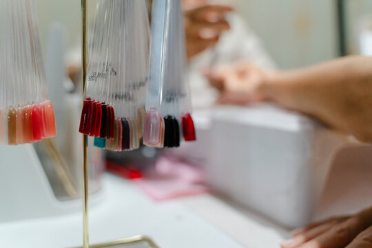 Colorful Nail Polish Swatches Displayed in a Beauty Salon During a Manicure Session with a Client's Hand Visible in Background