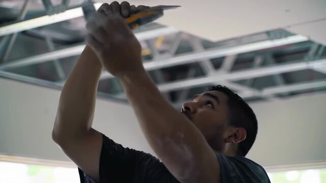 Construction worker installing ceiling grid system with power drill.