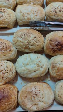 Vertical video of freshly baked puff pastries displayed in a bakery tray. The golden brown, flaky texture of the bread looks appetizing and crispy, ideal for food, bakery, and culinary-themed content.