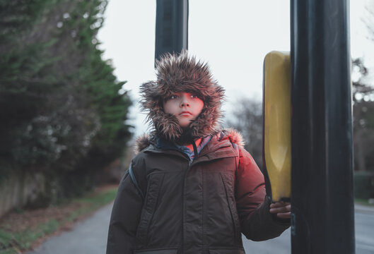 School child in warm winter coat pressing pedestrian button at crosswalk on chilly autumn morning, Kid boy waiting to cross street on way to school. Safety, daily routine, seasonal urban lifestyle