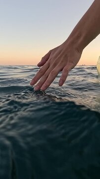 Hand water ocean, person touching calm sea at golden hour, tranquil nature. Vertical video.