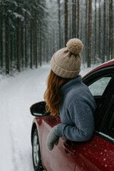 Winter road trip through snowy forest with woman in cozy hat leaning from red car
