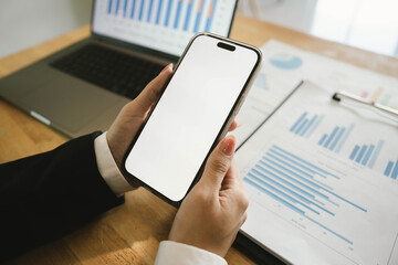 Businessperson analyzing financial charts using a calculator and laptop at a wooden desk, focusing on sales performance and data reports.