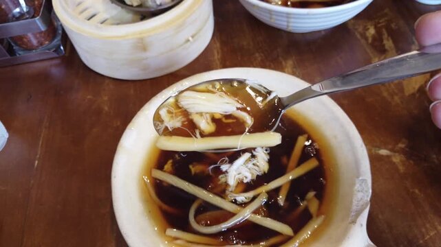 Delicious Thai-style braised fish maw soup served in a white bowl on a wooden table. Traditional Asian comfort food made with chicken, mushrooms, and thick brown broth, often found in street food stal