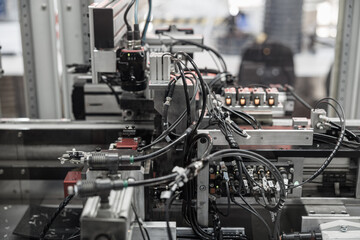 Complex industrial automation setup with densely packed black wiring, pneumatic connectors, and sensors integrated into a robotic processing line. Includes copy space