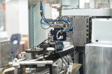 Industrial robotic unit with blue pneumatic and multi-colored electrical cables mounted on an automated production line for precision manufacturing tasks