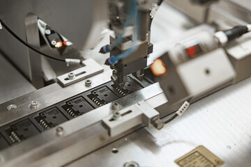 Precision robotic arm positioning electronic components onto black microchip carriers on an automated production line, with visible wiring and metallic guides