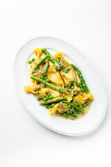 Gourmet stuffed pasta with asparagus, green peas, microgreens, and creamy yellow sauce, elegantly plated on a white dish. Fine dining presentation, top view.