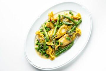 Gourmet stuffed pasta with asparagus, green peas, microgreens, and creamy yellow sauce, elegantly plated on a white dish. Fine dining presentation, top view.