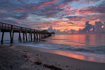 Fototapeta premium Serene Sunrise at Juno Beach: Pier Embraces the Ocean and Sky in Harmony