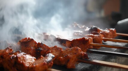 Skewered grilled meat (kebab) cooking on a smoky barbecue grill.