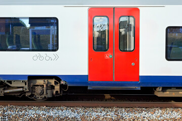 Obraz premium Modern train car with bright red doors on tracks, featuring accessibility symbols for bicycle and wheelchair passengers. Emphasizes public transport and travel.