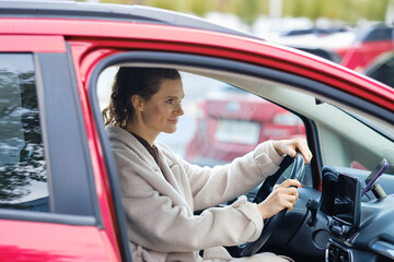 Woman driving a red car in a parking lot, showing focus and readiness on a busy day