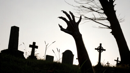 Graveyard scene with a hand reaching up from the ground at dusk showing eerie silhouettes of tombstones