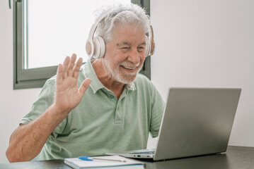 Video call concept.  Senior caucasian businessman with headphones smiling working online on laptop, in remote working waving hand