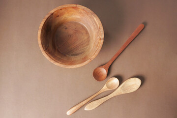 A wooden bowl and a wooden spoon are placed on a brown background.