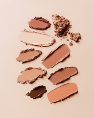 Vertical group of loose eyeshadow swatches on pastel brown background. Monochrome close-up of cosmetics texture, natural skin colors. Professional studio light