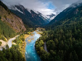 A breathtaking aerial view of a vibrant blue river winding through a lush green valley, flanked by towering mountains partially shrouded in mist.