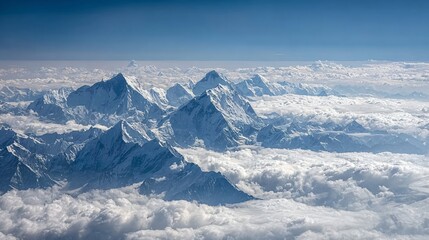 A breathtaking aerial view of snow-capped mountain peaks rising majestically above a sea of clouds under a clear blue sky.