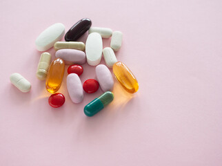 A collection of supplements of various pills and capsules scattered on a light pink background. Close-up with copy space. Health supplement concept.