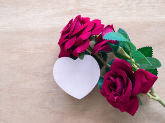 Pink heart shaped card with red roses on wooden background. Love, Anniversary, Valentine's Day card concept. Top view, flat lay with copy space.