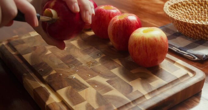 Close-up of hands coring fresh red apples on a wooden cutting board as they prepare ingredients for a homemade dessert in the warm, natural light of a kitchen.