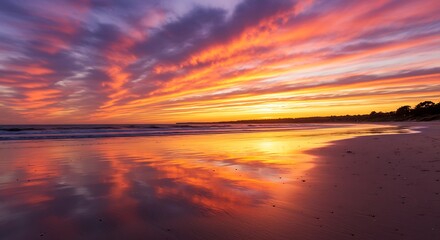 Vibrant sunset sky reflecting on wet sand of empty beach landscape