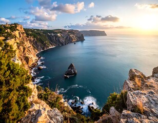 Fototapeta premium Coastal view featuring rugged cliffs, deep blue ocean, a solitary rock island, and a bright sunset with clouds