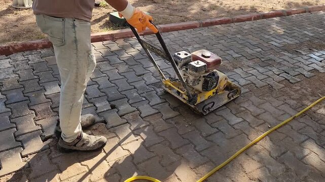A worker using a plate compactor to flatten the pavement surface after installation