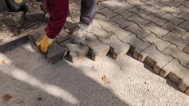 A paver laying the interlocking pavement stones to floor at a walkway construction site