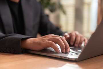 Close-up of male hands typing on laptop keyboard at wooden desk in office. Professional business environment, modern workspace concept, remote work, productivity, and digital communication.