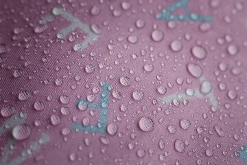 Fresh clear water droplets bead perfectly vibrant pink waterproof fabric surface, creating beautiful textured pattern. Tiny liquid spheres reflect light, conveying sense of refreshing purity