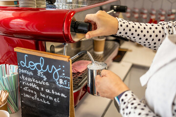Barista preparing coffee in a coffee machine. The handwritten menu has the following inscription in Polish: Ice cream, portion 85g, strawberry, ricotta with elderberry, salted caramel, cream

