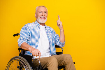 Cheerful grandpa in a wheelchair points to a bright idea while smiling against a bold yellow background bringing hope and humor to rehab and everyday health