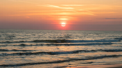 Obraz premium Vibrant sunset over the ocean, with warm hues of orange and red illuminating the water.