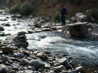 Solitary man carefully crossing a unique, rustic stone bridge over a clear flowing river in a serene, wild natural landscape.