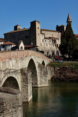 Obraz premium Monastero Bormida in Piedmont, Italy. An ancient Italian town with a historic stone bridge over the river surrounded by spring greenery. A peaceful and scenic landscape rich in heritage.