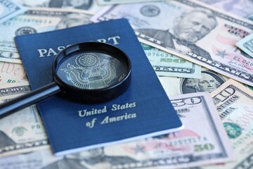 US passport and magnifying glass on the background of many dollar bills close up