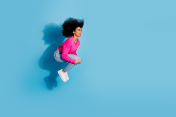 Obraz premium Joyful young woman in a vibrant pink sweater against a blue background, embracing carefree moments with a wide smile