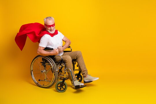 Funny senior superhero in wheelchair cape and mask smiles on bold yellow backdrop bringing hope and humor